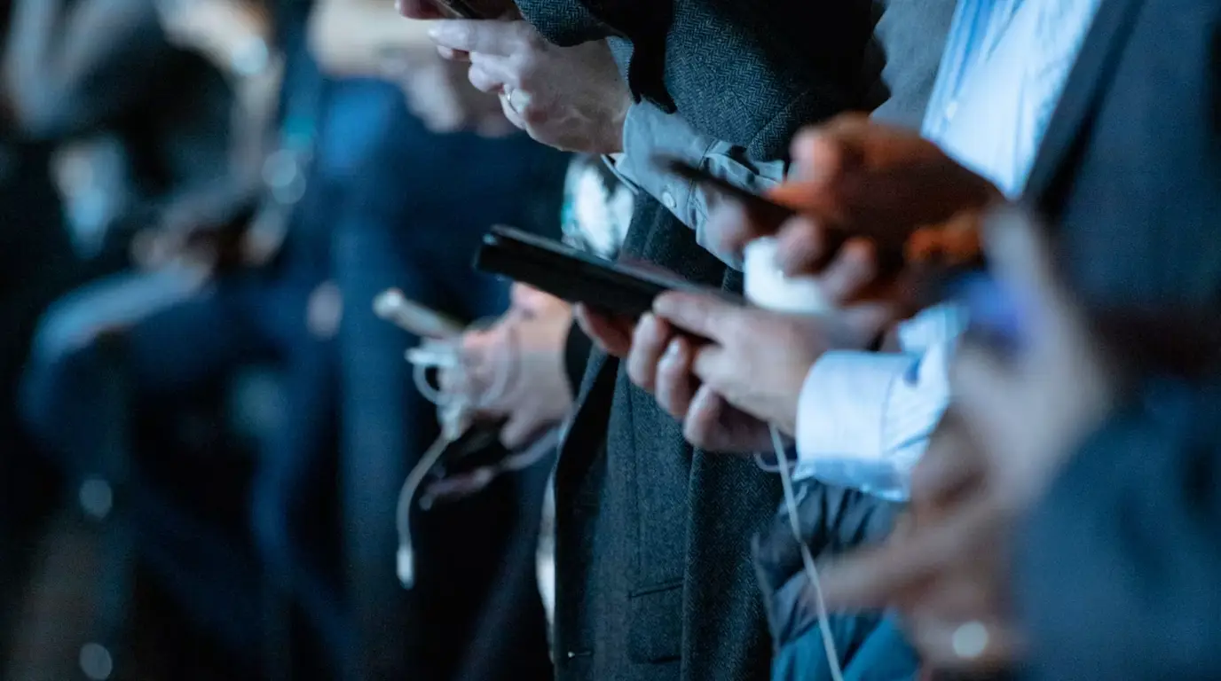 Crowd of people using their phones in an event room cast by a blue light.