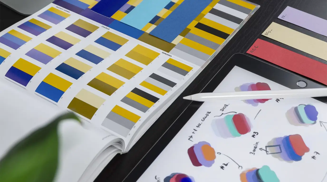 Books of color swatches and an Apple Pencil on a dark design.