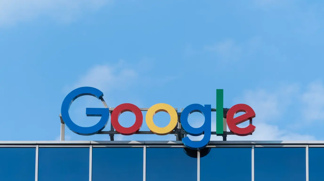 A Google sign on a glass building against a blue sky with light cloud coverage.