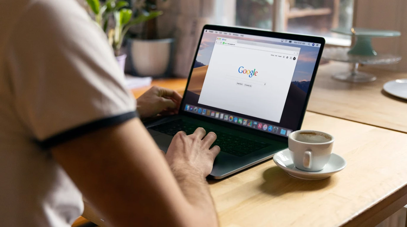 A photograph from behind a person sitting at a desk with a laptop open to Google in a browser window.