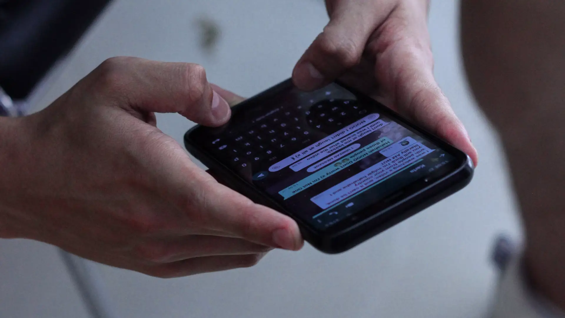 Two hands typing on a phone displaying a WhatsApp message thread.